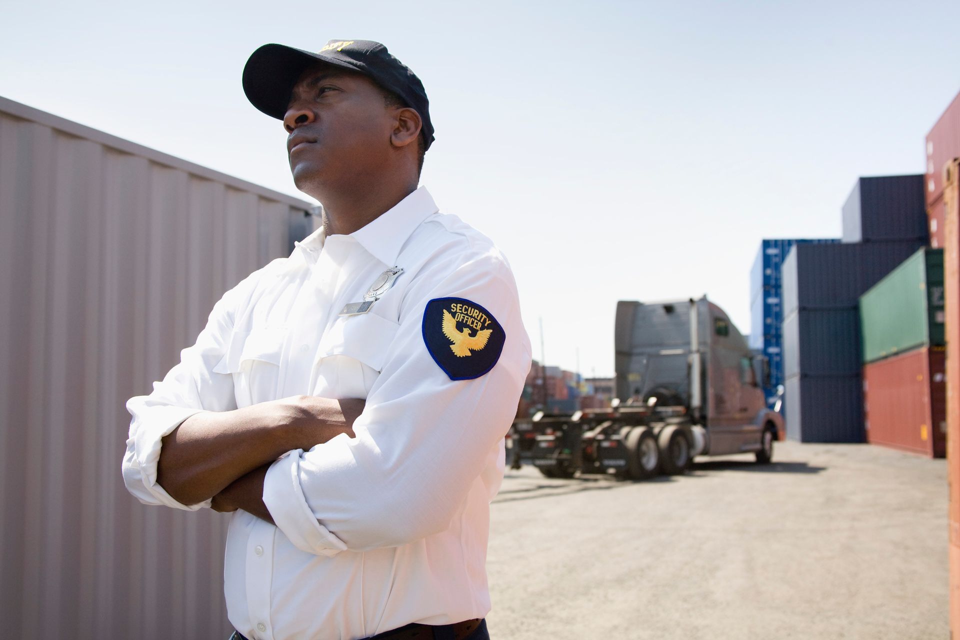 A security guard stands in front of a truck with his arms crossed