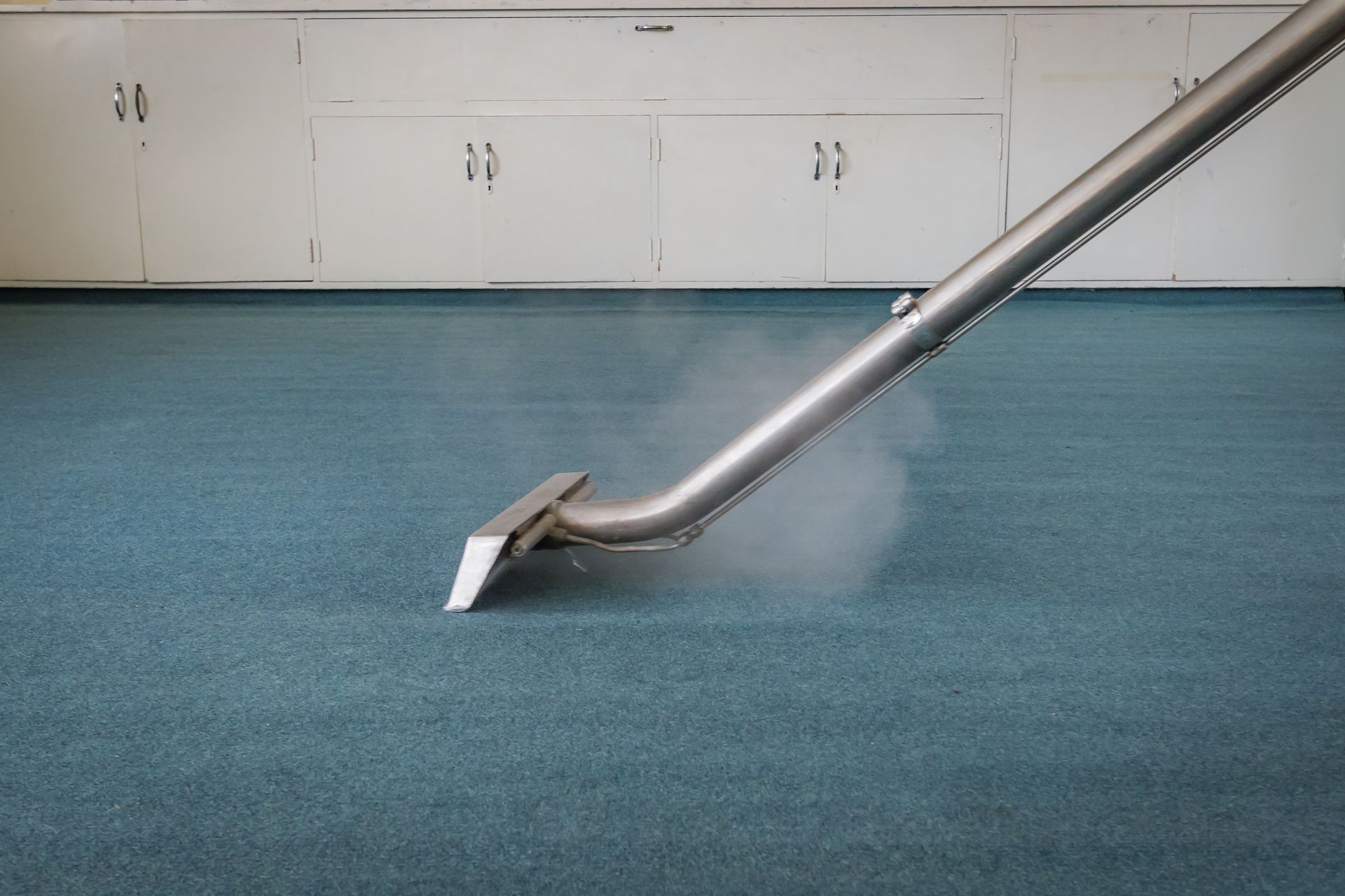 A vacuum cleaner is cleaning a blue carpet in a room.