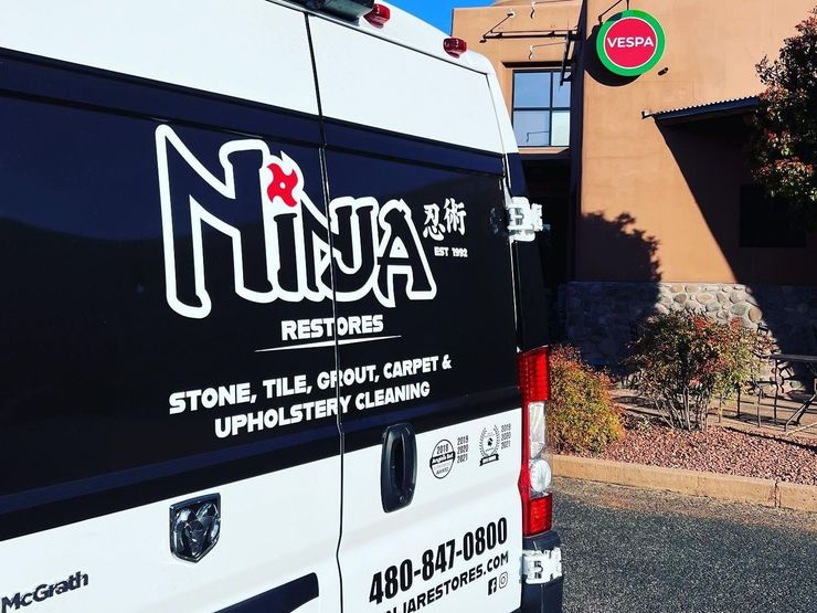 A white van with the word ninja restores on the back is parked in front of a building.