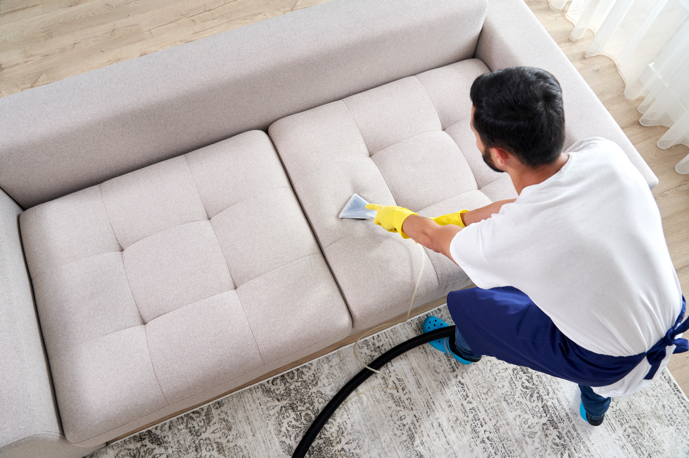 A man is cleaning a couch with a vacuum cleaner.