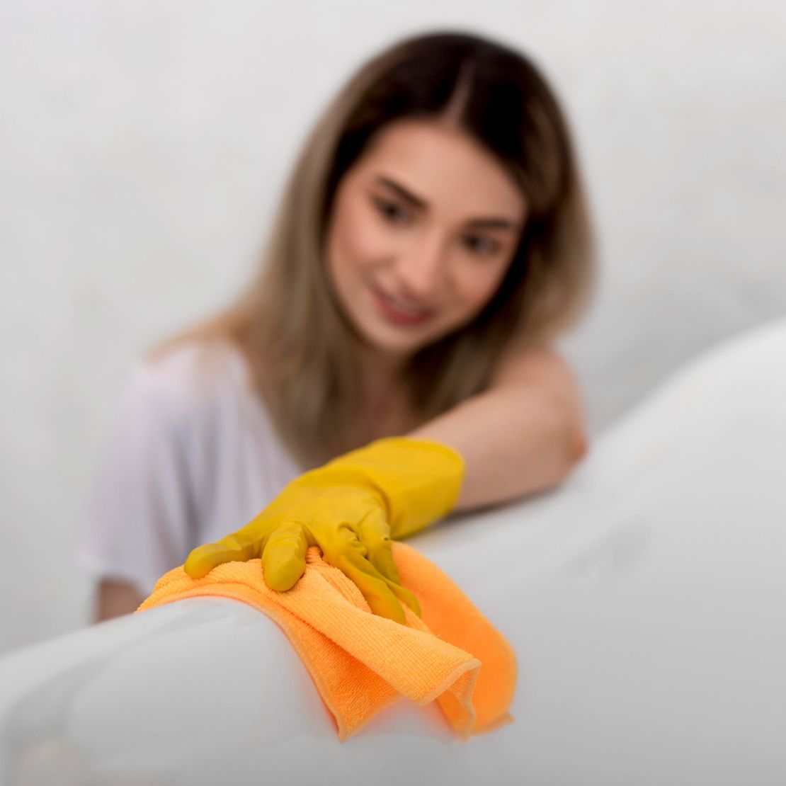 A woman is cleaning a bathtub with a towel and gloves.