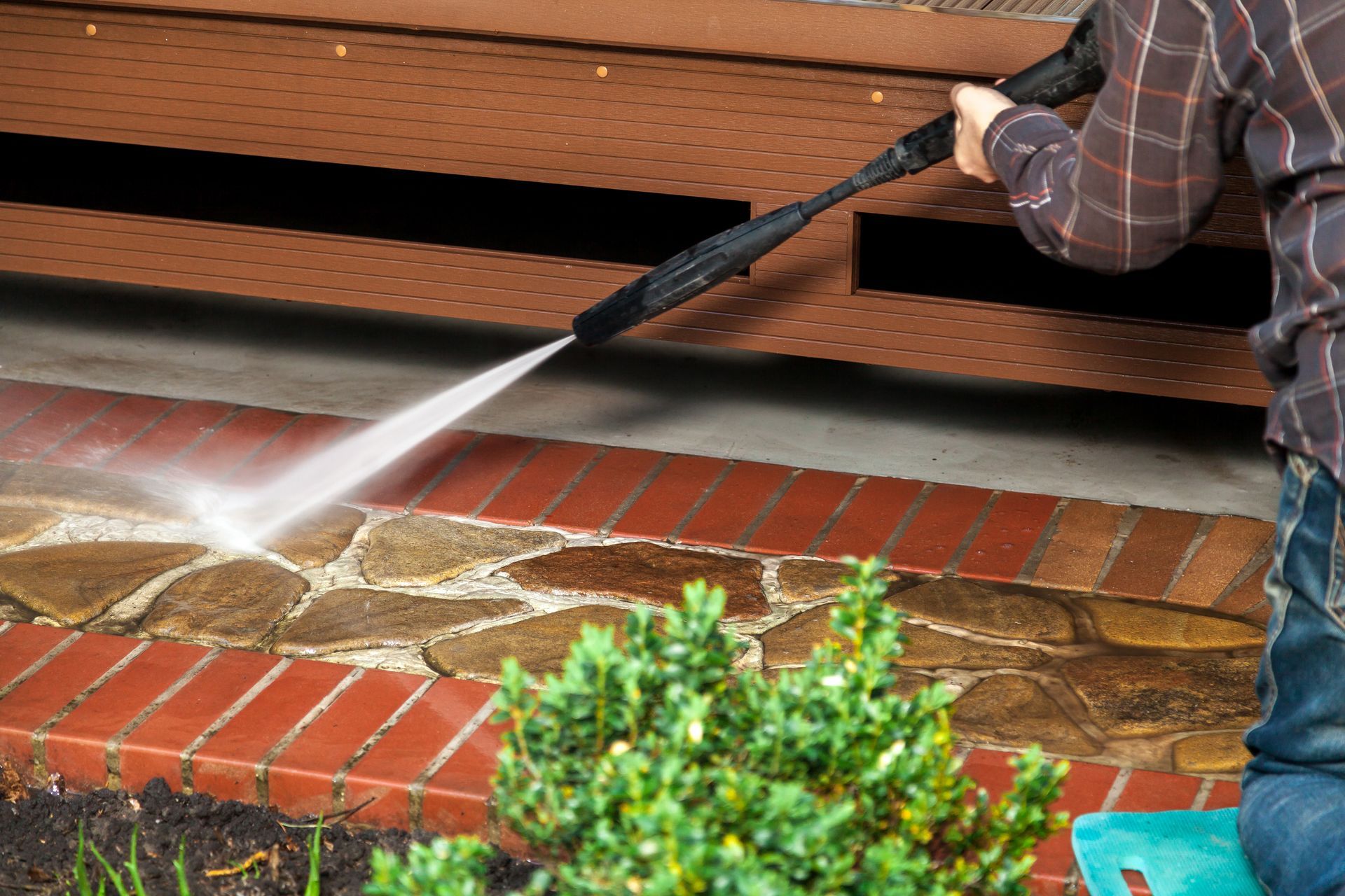 A man is using a high pressure washer to clean a brick walkway.