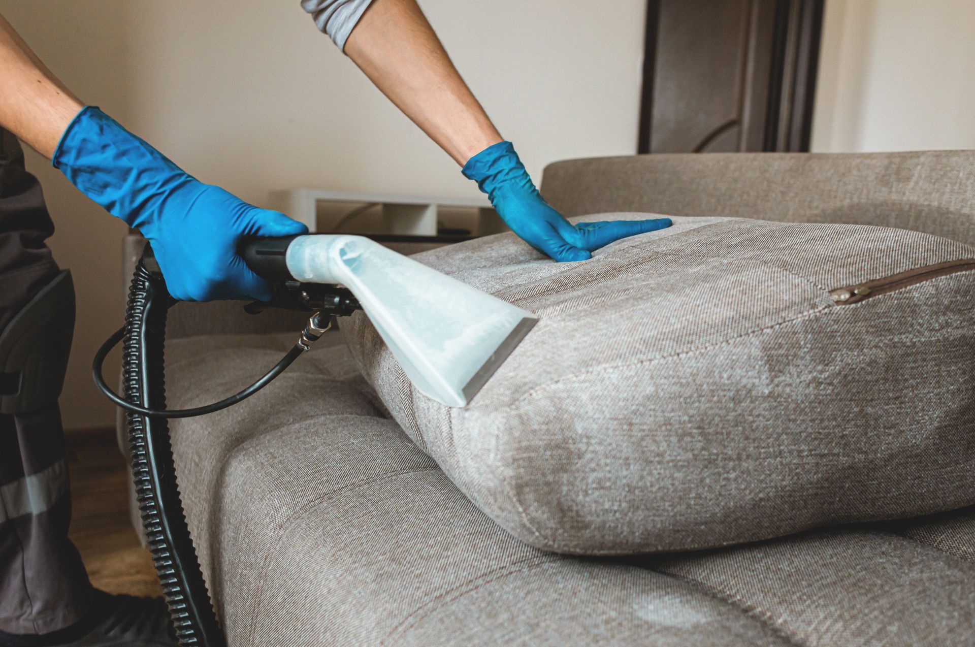 A person is cleaning a couch with a vacuum cleaner.