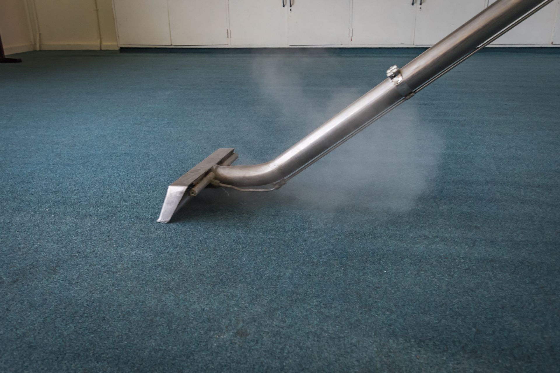 A vacuum cleaner is cleaning a blue carpet in a room.