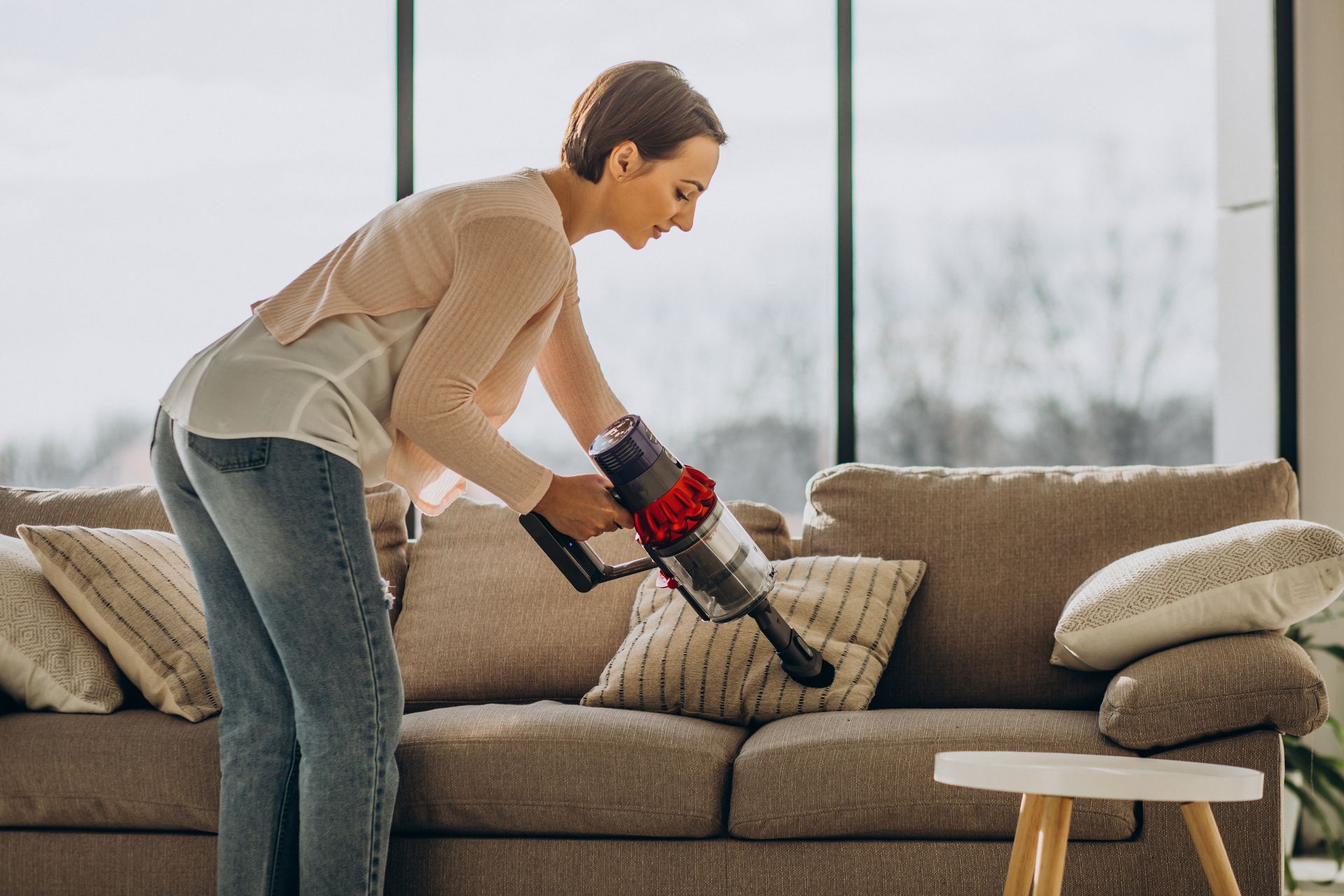 A woman is cleaning a couch with a vacuum cleaner.