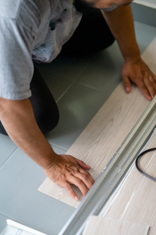 A Man Is Kneeling On The Floor While Installing A Wooden Floor — Norm Evans Floors Pty Ltd in Noosa, QLD