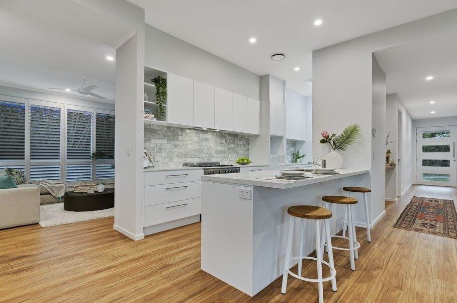 A Kitchen With White Cabinets And Wooden Floors And Stools  — Norm Evans Floors Pty Ltd in Kunda Park, QLD