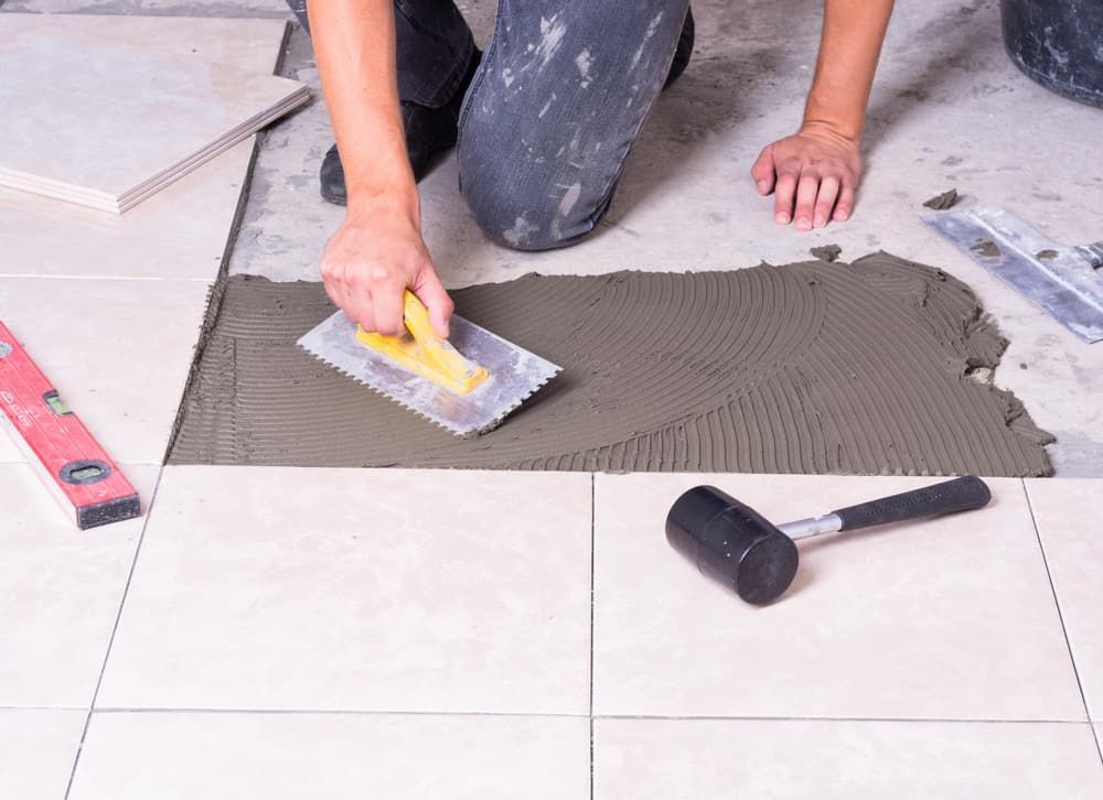 A Person Is Laying Tiles On The Floor With A Trowel — Norm Evans Floors Pty Ltd in Nambour, QLD