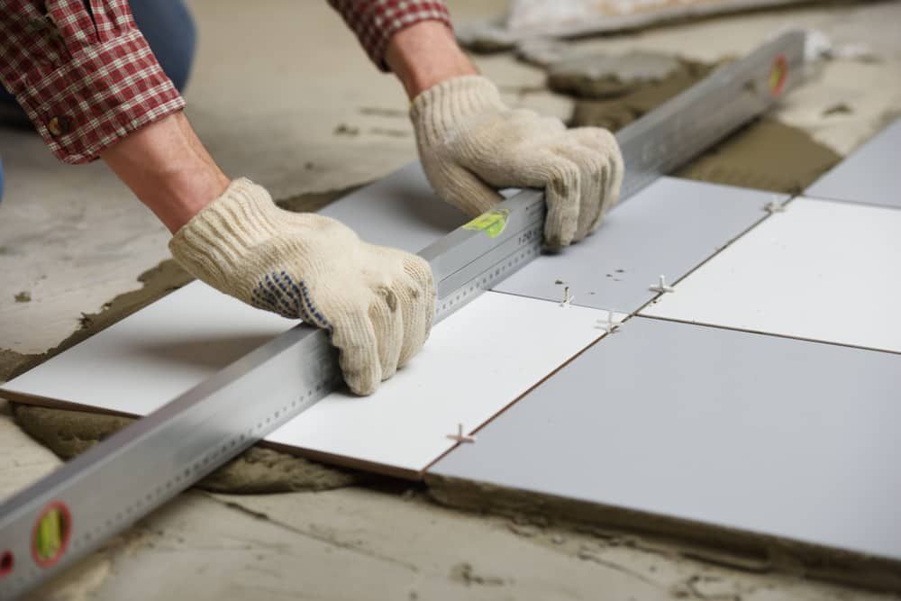 A Man Is Measuring A Tile Floor With A Level — Norm Evans Floors Pty Ltd in Beerwah, QLD
