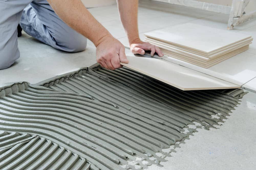 A Person Is Laying Tiles On A Tiled Floor — Norm Evans Floors Pty Ltd in Beerwah, QLD