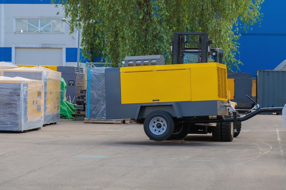 A Yellow And Gray Air Compressor Is Being Towed By A Forklift In A Parking Lot — Hybrid Power Australia In Tieri, QLD