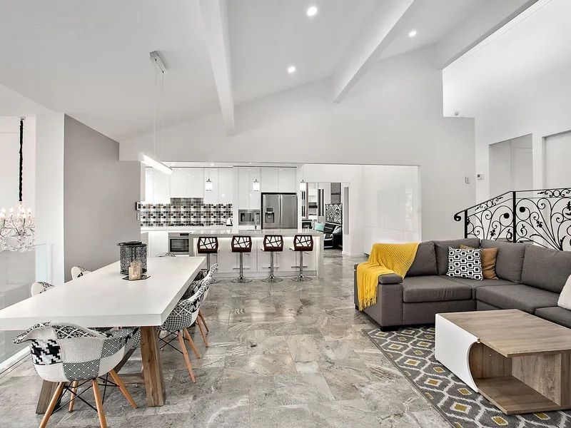 Open-concept living space with gray sectional, white dining table, and kitchen with bar stools — Corrimal Discount Tiles and Bathroomwear in East Corrimal, NSW