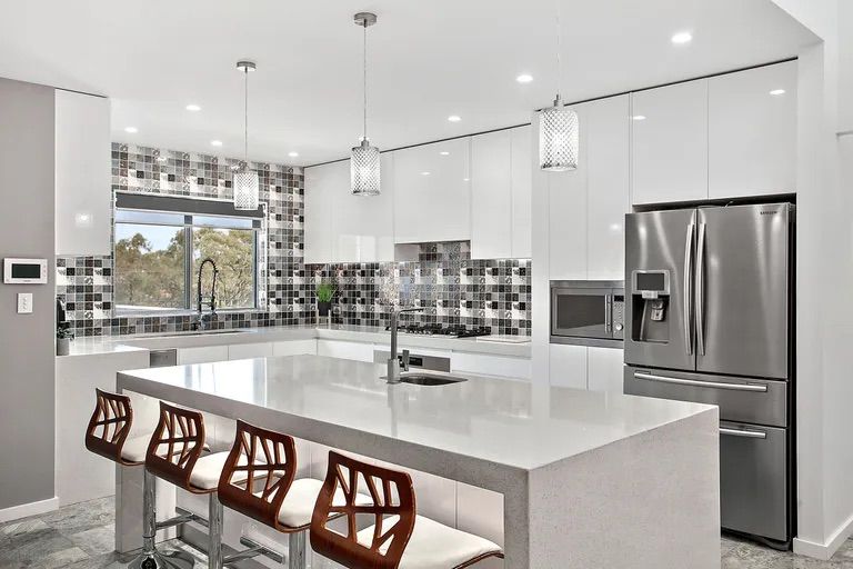 Modern white kitchen with island, stainless steel appliances, and decorative backsplash; four bar stools — Corrimal Discount Tiles and Bathroomwear in East Corrimal, NSW