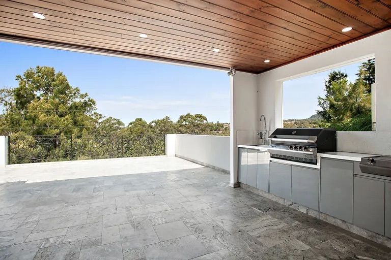 Outdoor kitchen with a built-in grill, sink, and countertop. Views of trees from the patio — Corrimal Discount Tiles and Bathroomwear in East Corrimal, NSW