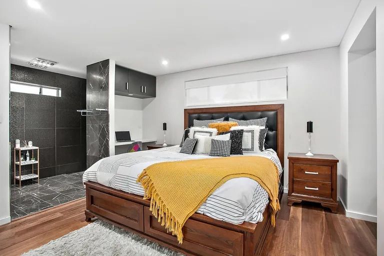Bedroom with dark wood bed, yellow blanket, and small bathroom, featuring dark tile — Corrimal Discount Tiles and Bathroomwear in East Corrimal, NSW