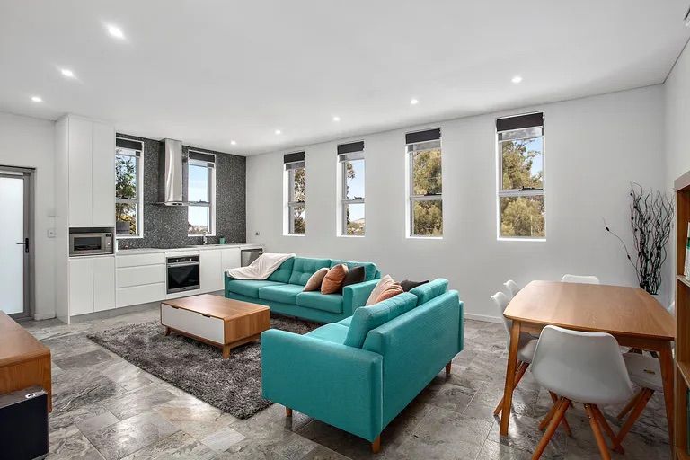 Spacious modern living area with teal sofas, kitchen, dining table, and large windows — Corrimal Discount Tiles and Bathroomwear in East Corrimal, NSW