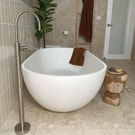 A White Bathtub is Sitting in a Bathroom Next to a Wooden Stool — Corrimal Discount Tiles and Bathroomwear in East Corrimal, NSW
