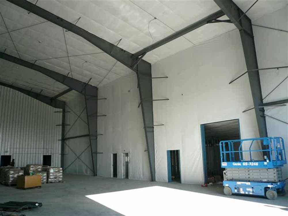 Interior of a large warehouse with steel beams, white walls, and a blue lift.