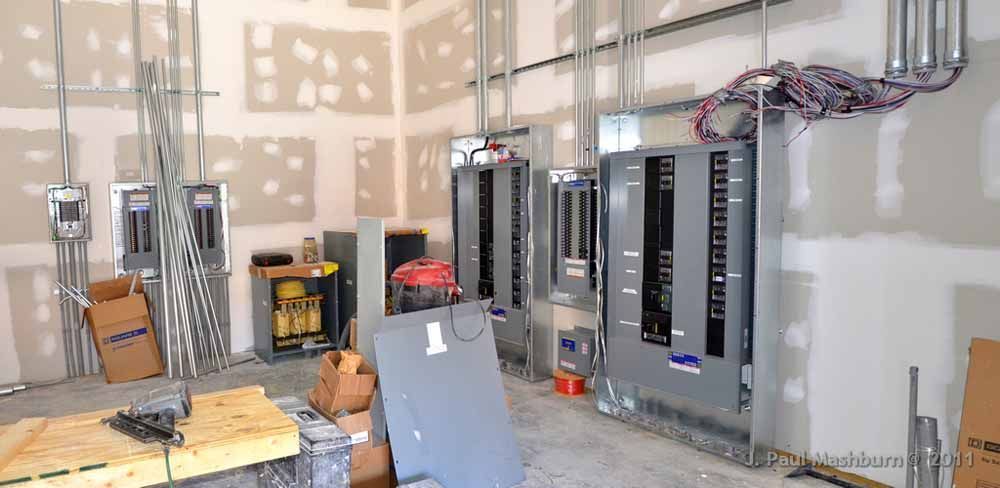 Electrical panels and conduit in a construction setting with drywall and unfinished walls.