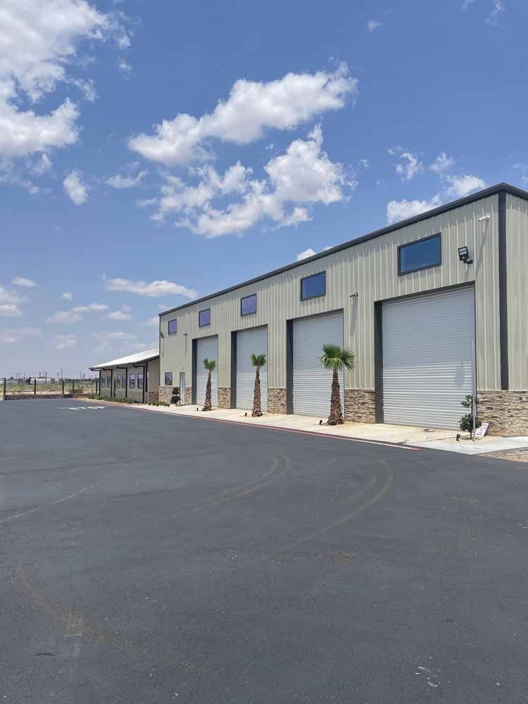 Gray metal building with four garage doors, palm trees, and blue sky.