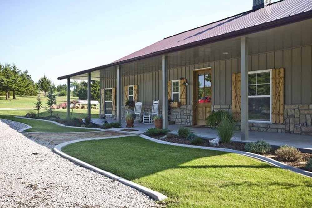 A house with a long porch and a gravel driveway, surrounded by green grass and landscaping.
