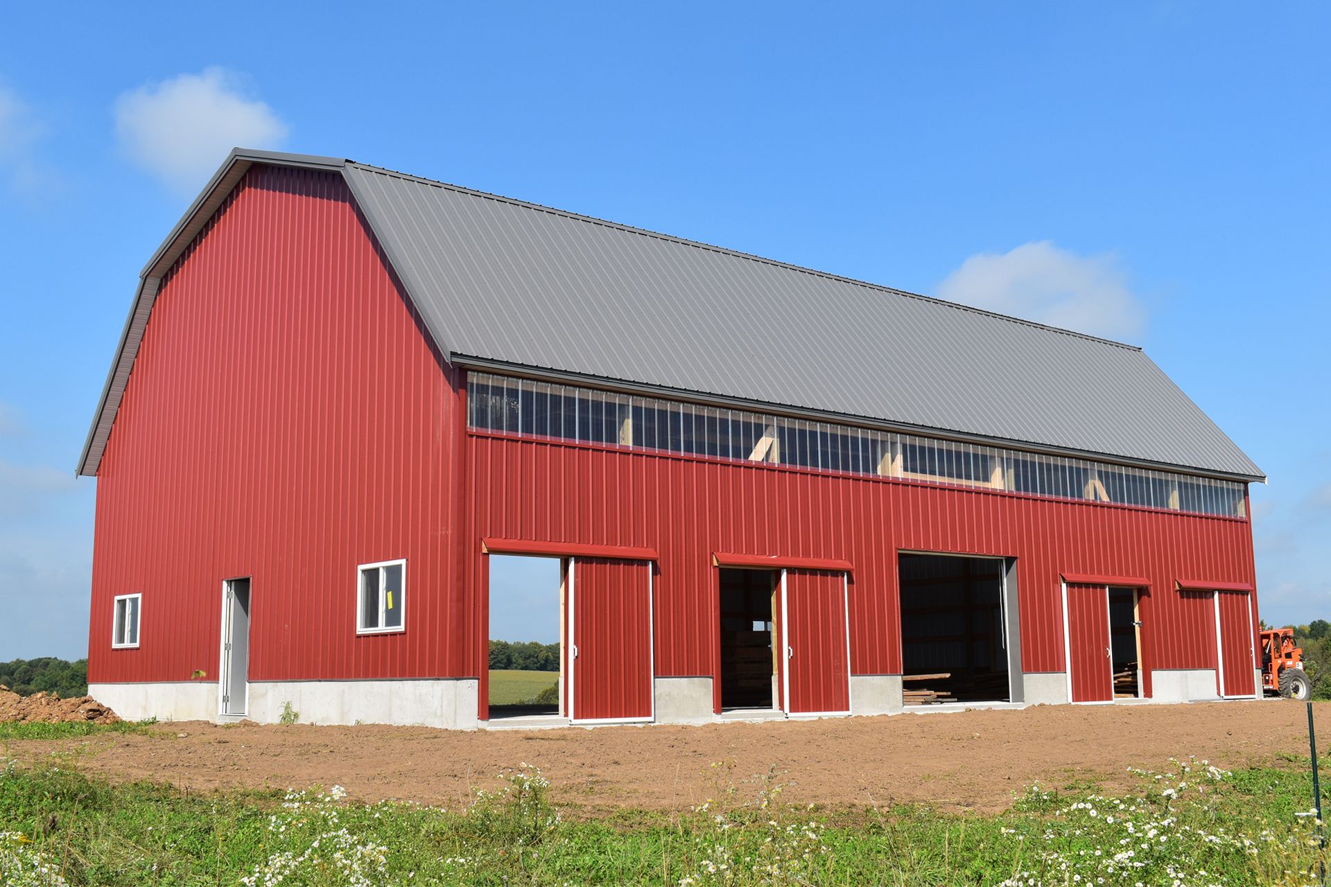 Red barn with gray roof, multiple sliding doors, and windows, set against a blue sky.