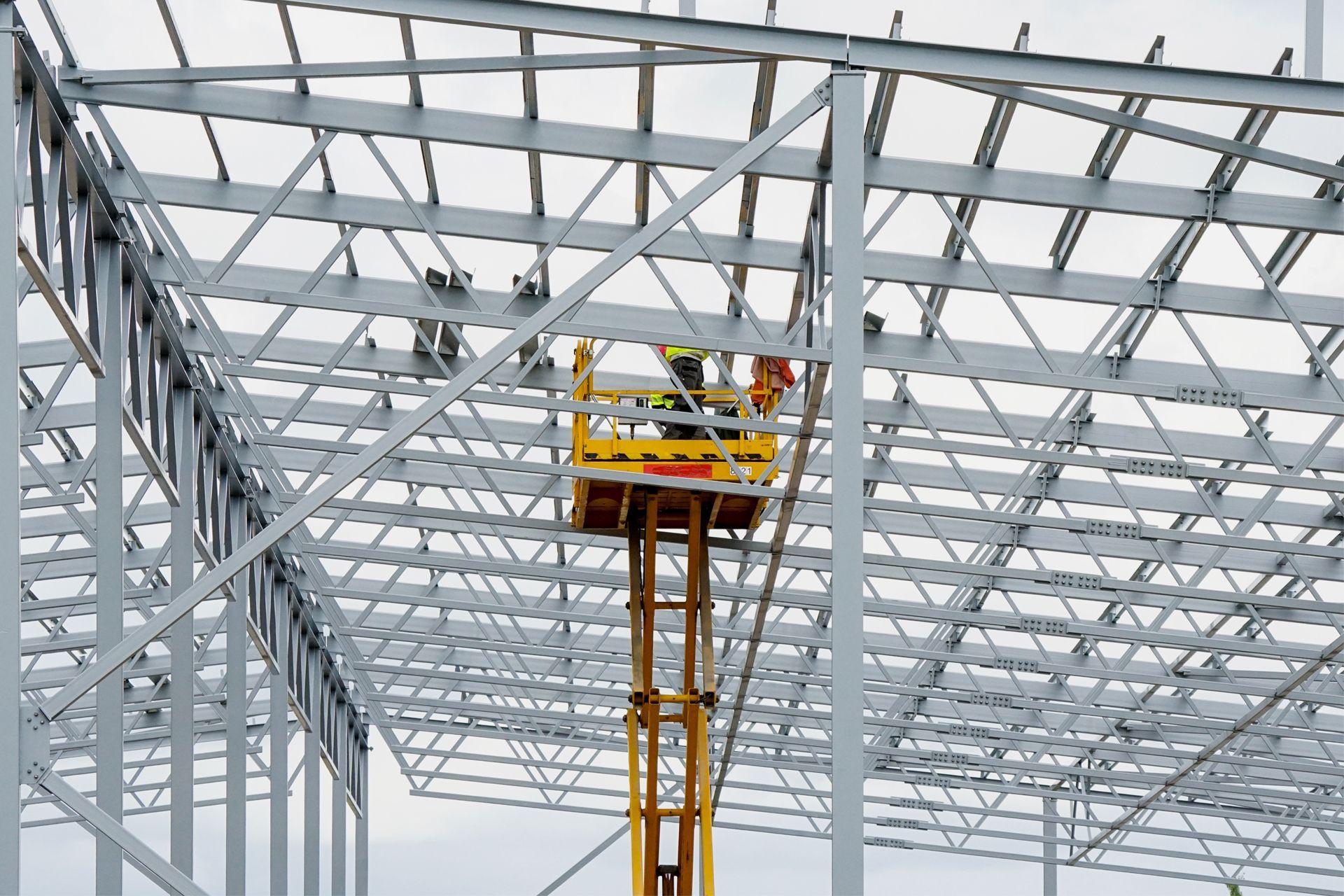 Construction workers in a lift platform, building a steel-framed industrial building.