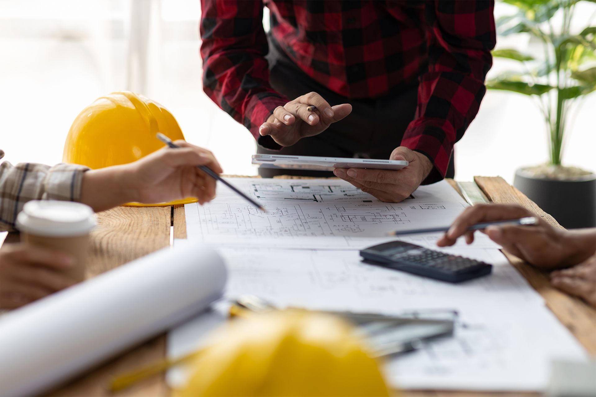Engineers at a table review blueprints with a tablet and pencils.