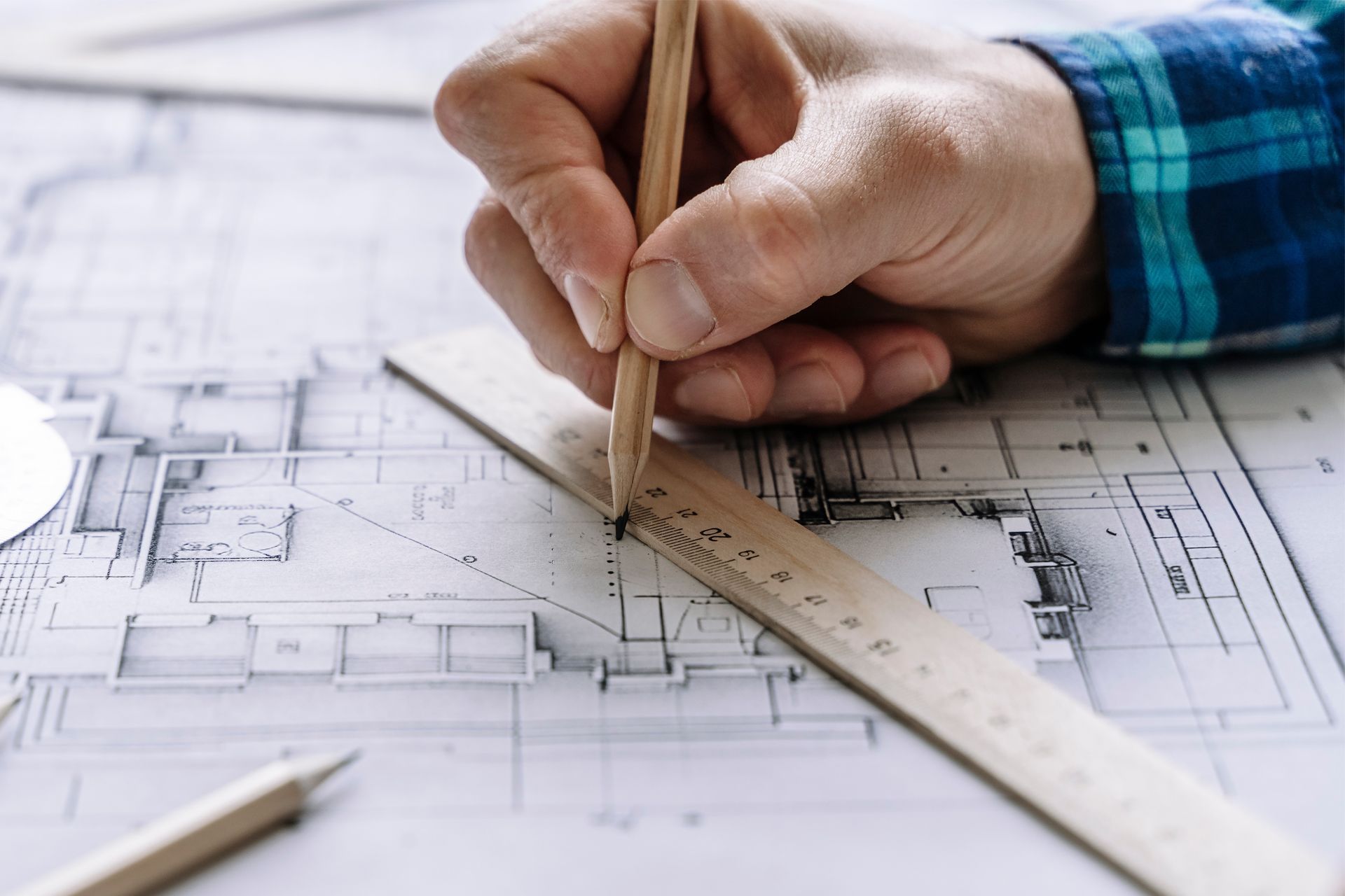 Hand using a pencil and ruler to draw on architectural blueprints.