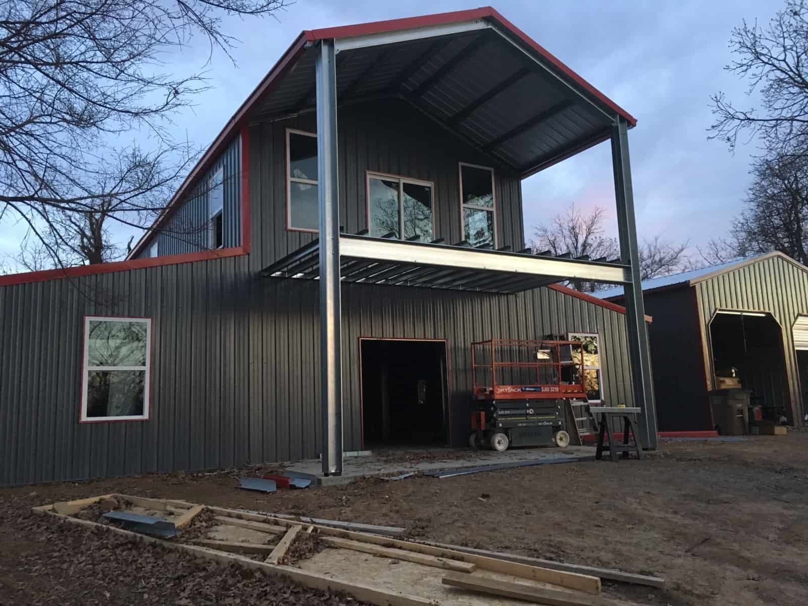Two-story gray metal building with a red roof; a lift and open doorway visible.