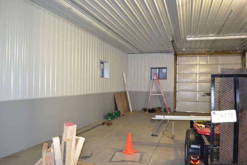 Interior of a workshop with white and gray walls, a closed garage door, tools, and a ladder.