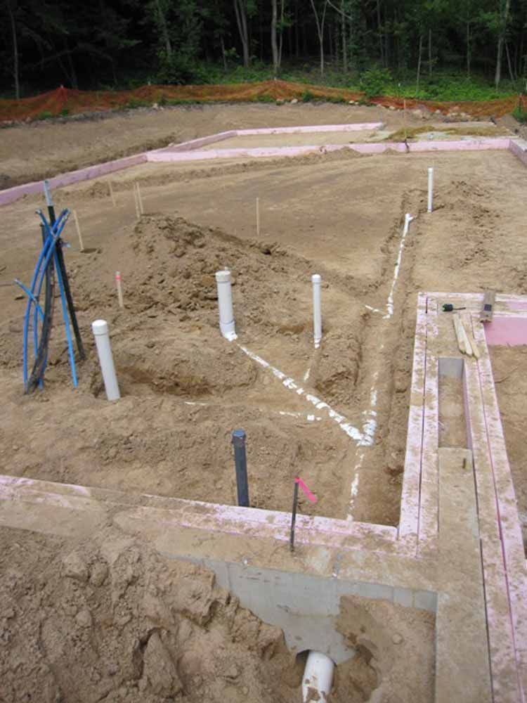 Construction site with white plumbing pipes laid out in sandy foundation.