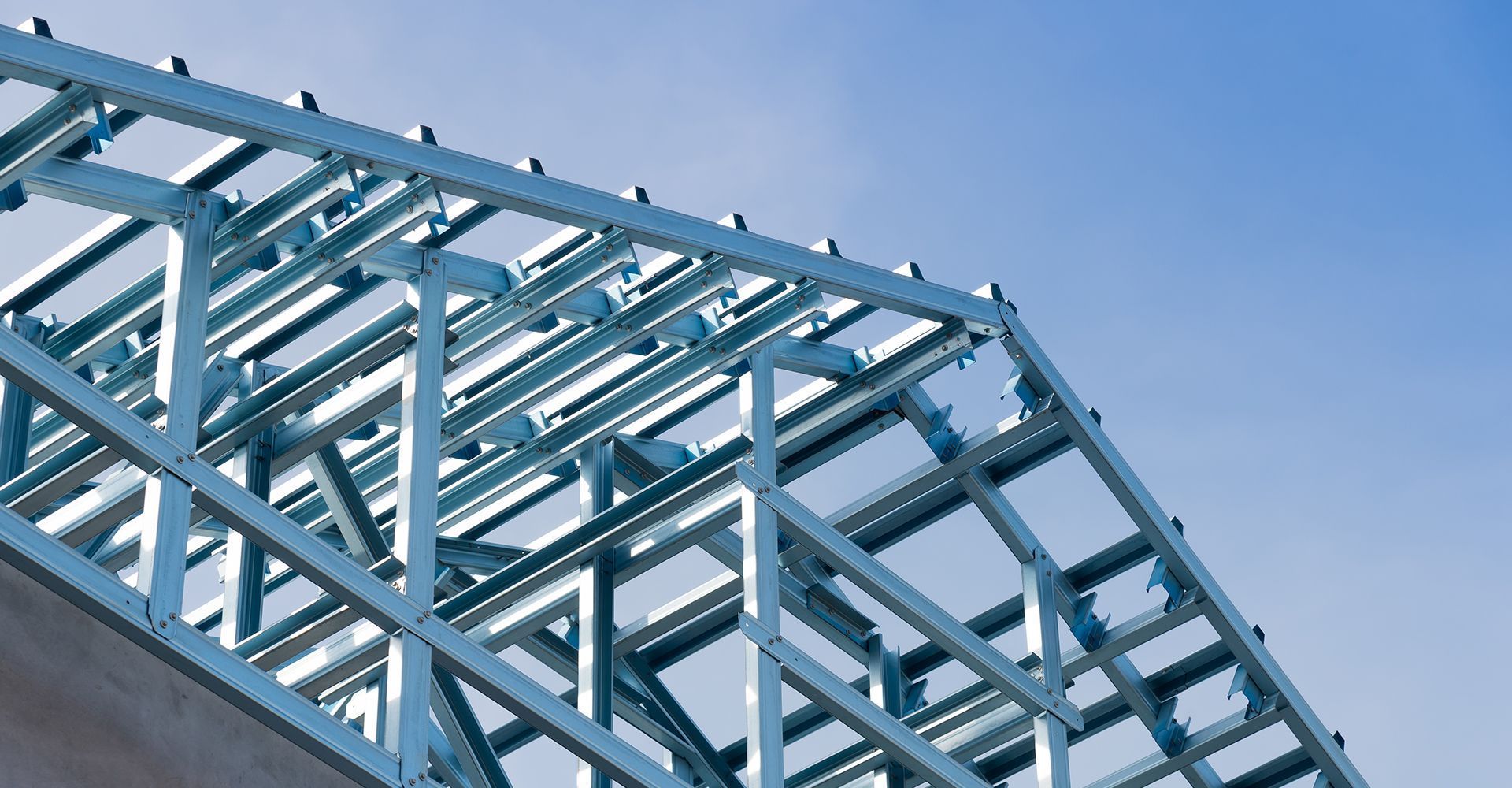 Blue metal roof trusses against a blue sky, partially built.