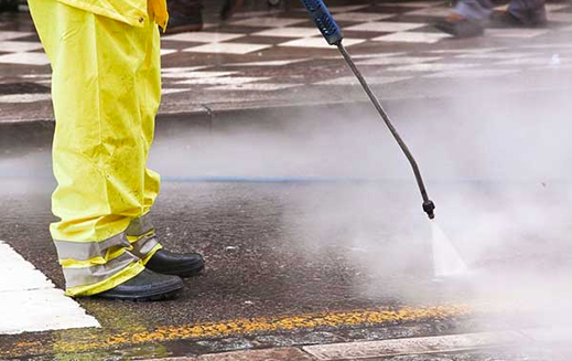 A person is using a high pressure washer to clean a sidewalk.