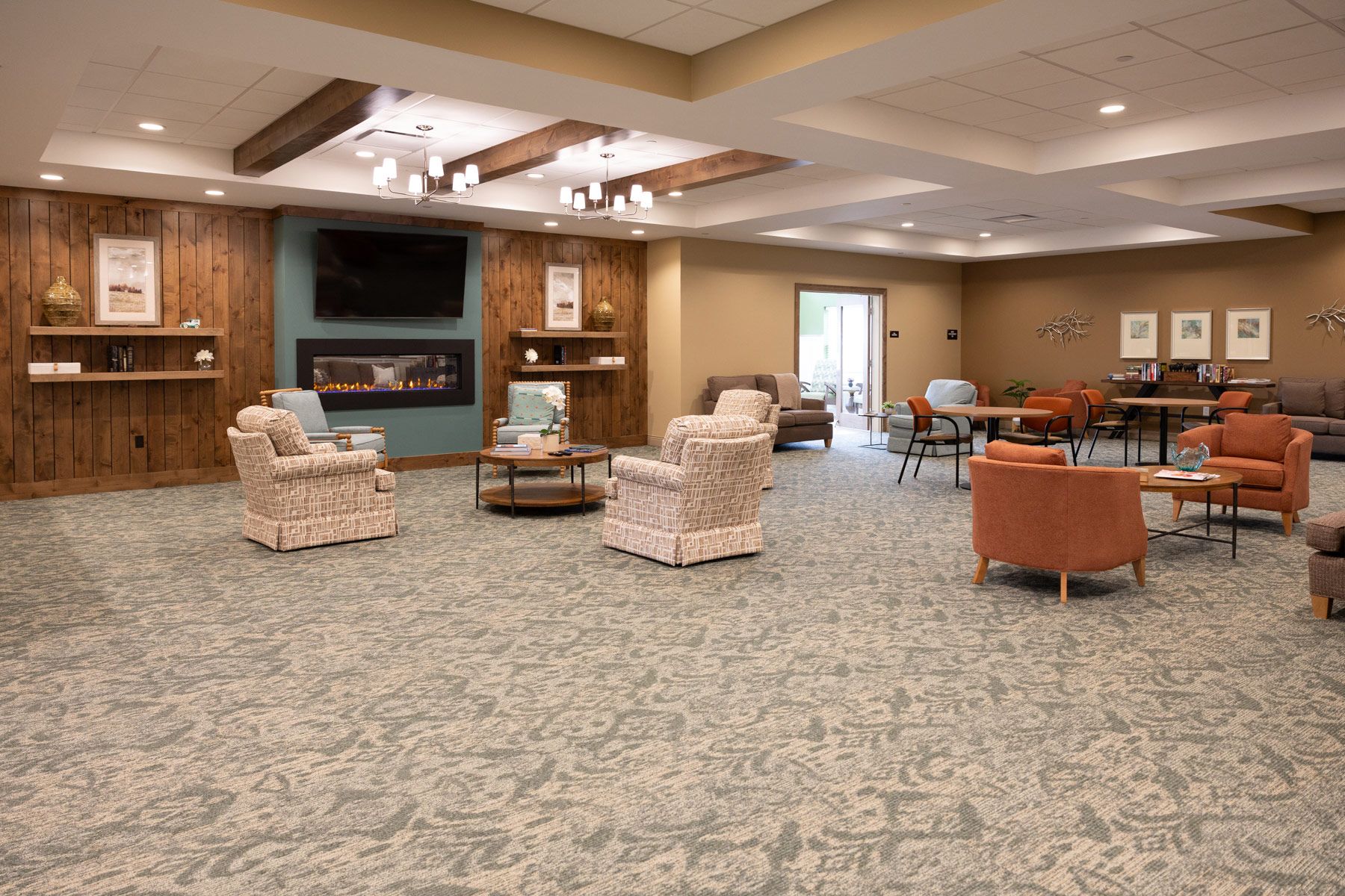 Spacious lounge with various armchairs, tables, and a fireplace. Neutral-toned walls and patterned carpet.