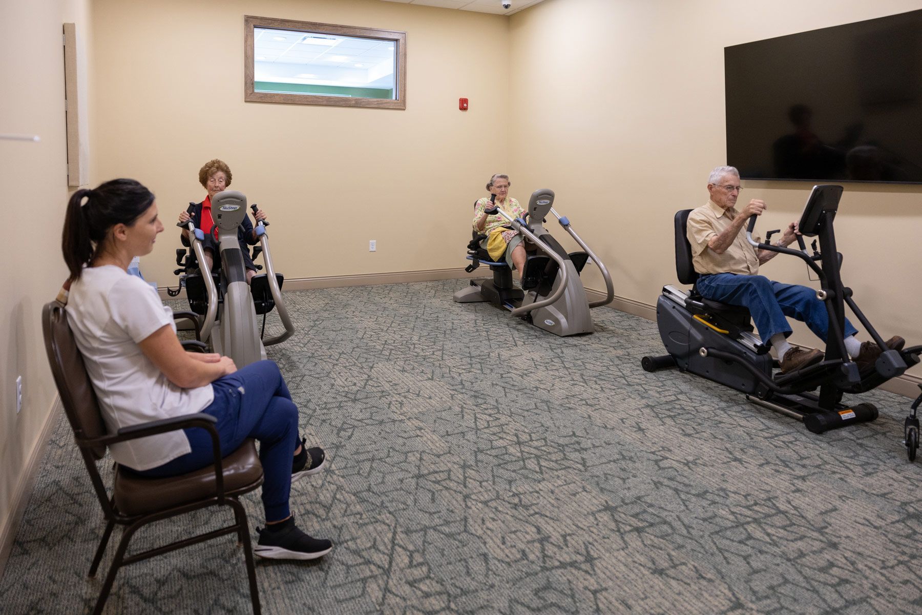 Woman watches three people using exercise machines in a room.
