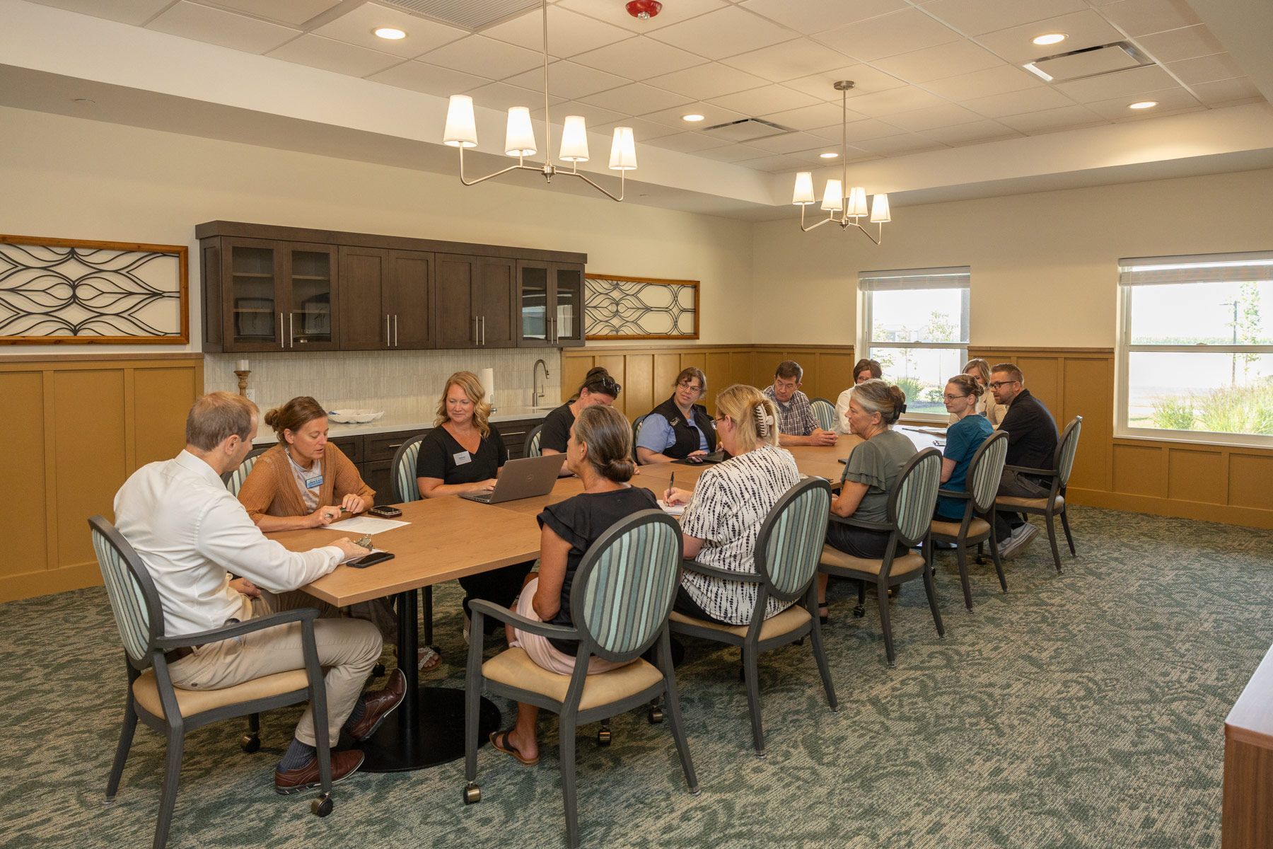 Group of people seated around a table in a meeting room with wood paneling and cabinetry.