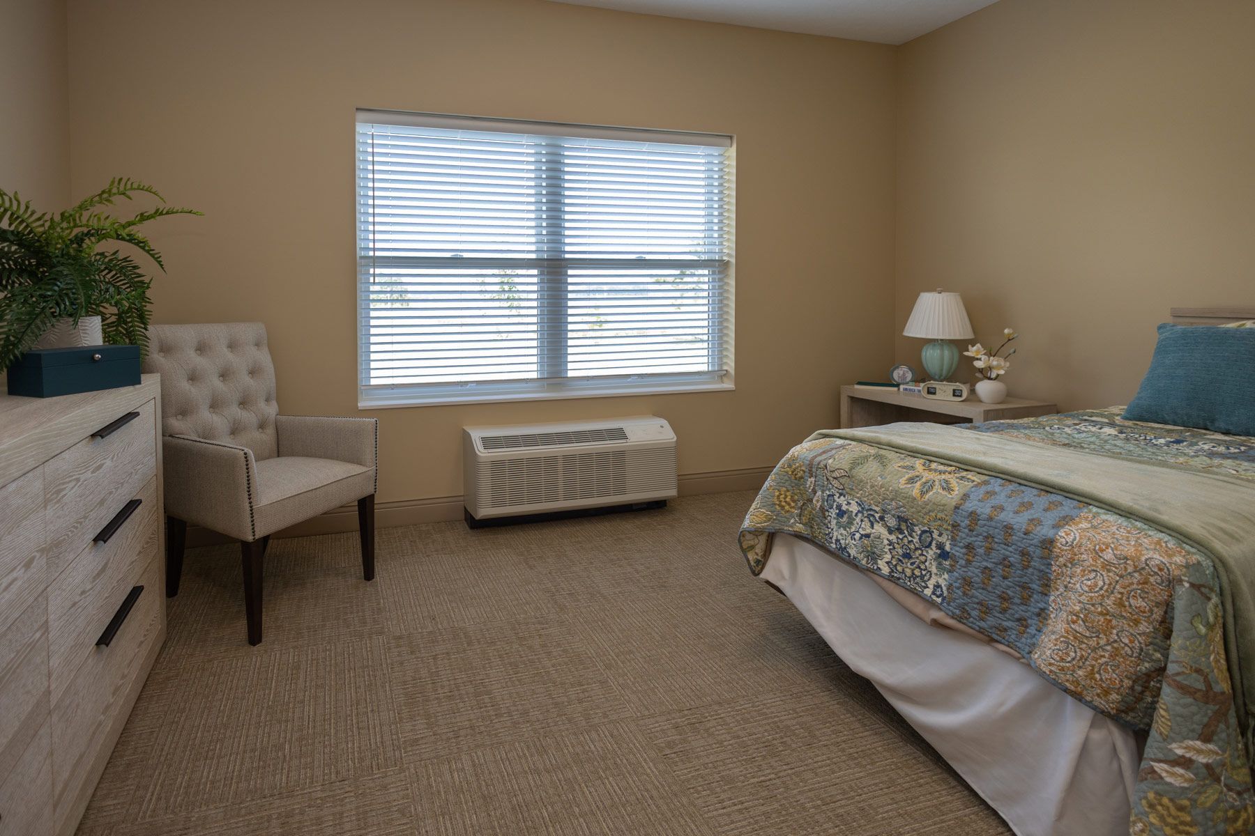 Bedroom with beige walls, carpet, window with blinds, bed, dresser, chair, and air conditioner.