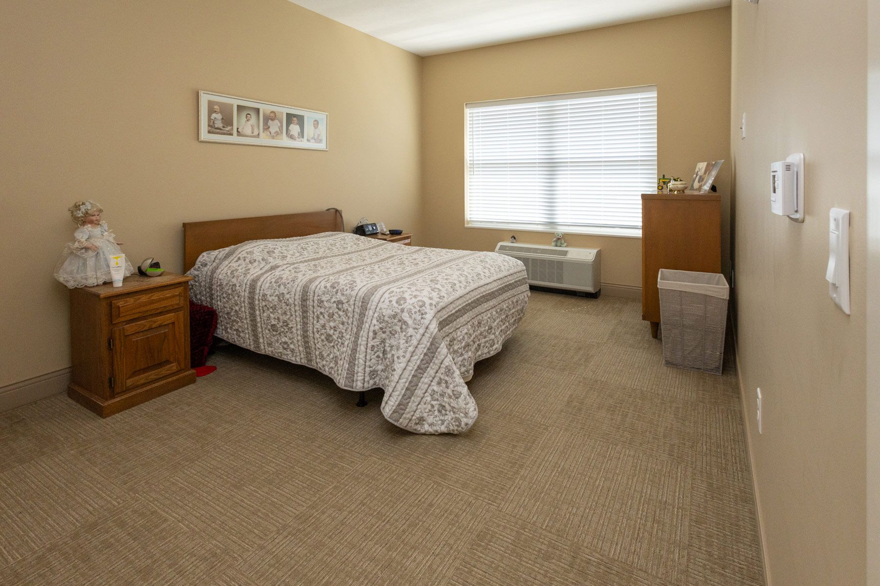 Bedroom with bed, nightstand, dresser, and window. Beige walls and carpet.