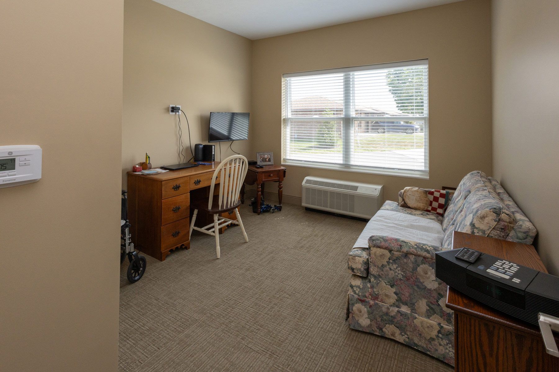 Small room with desk, chair, TV, sofa, window, and beige walls.