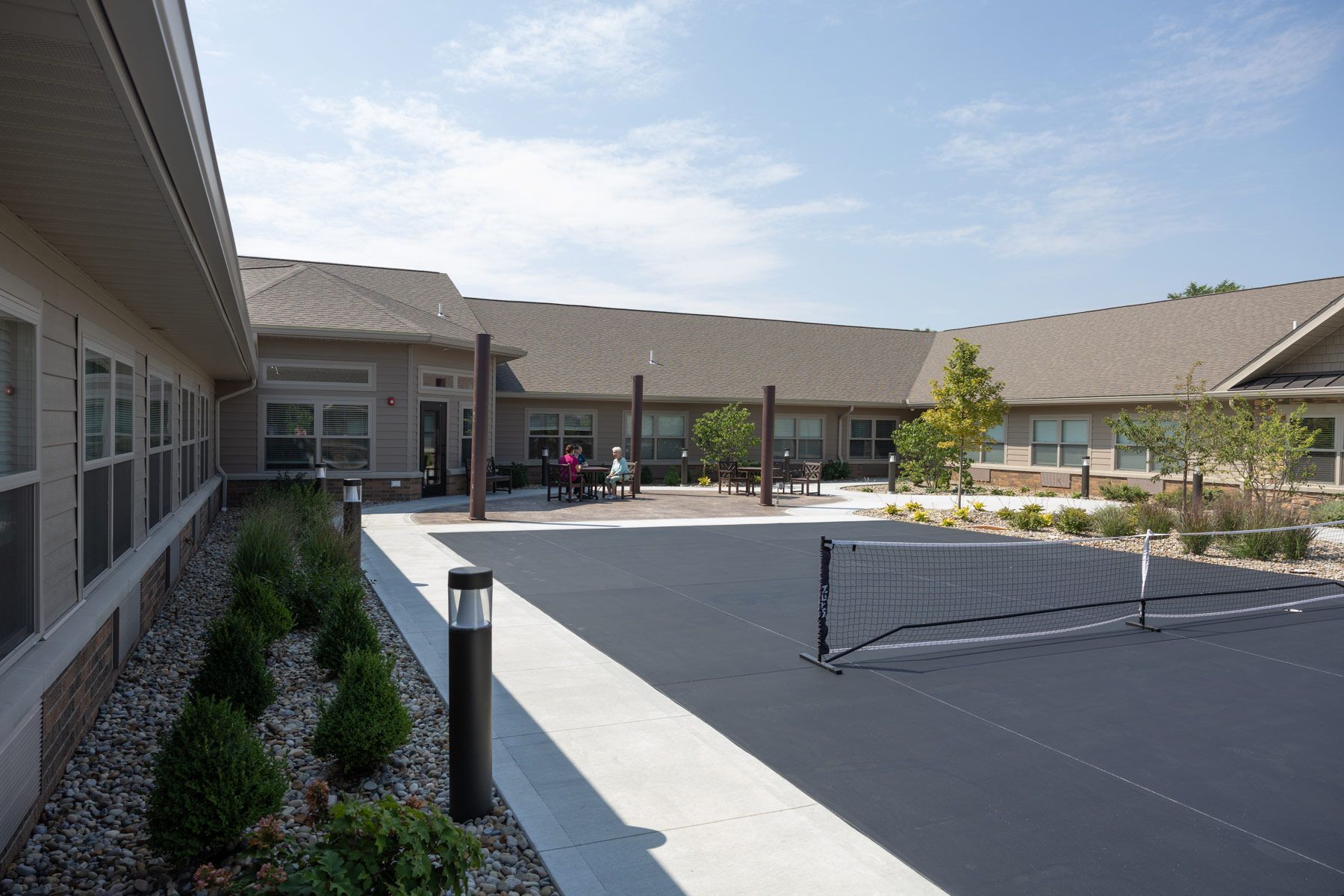 Courtyard with a tennis net, building, and a few people under a blue sky.