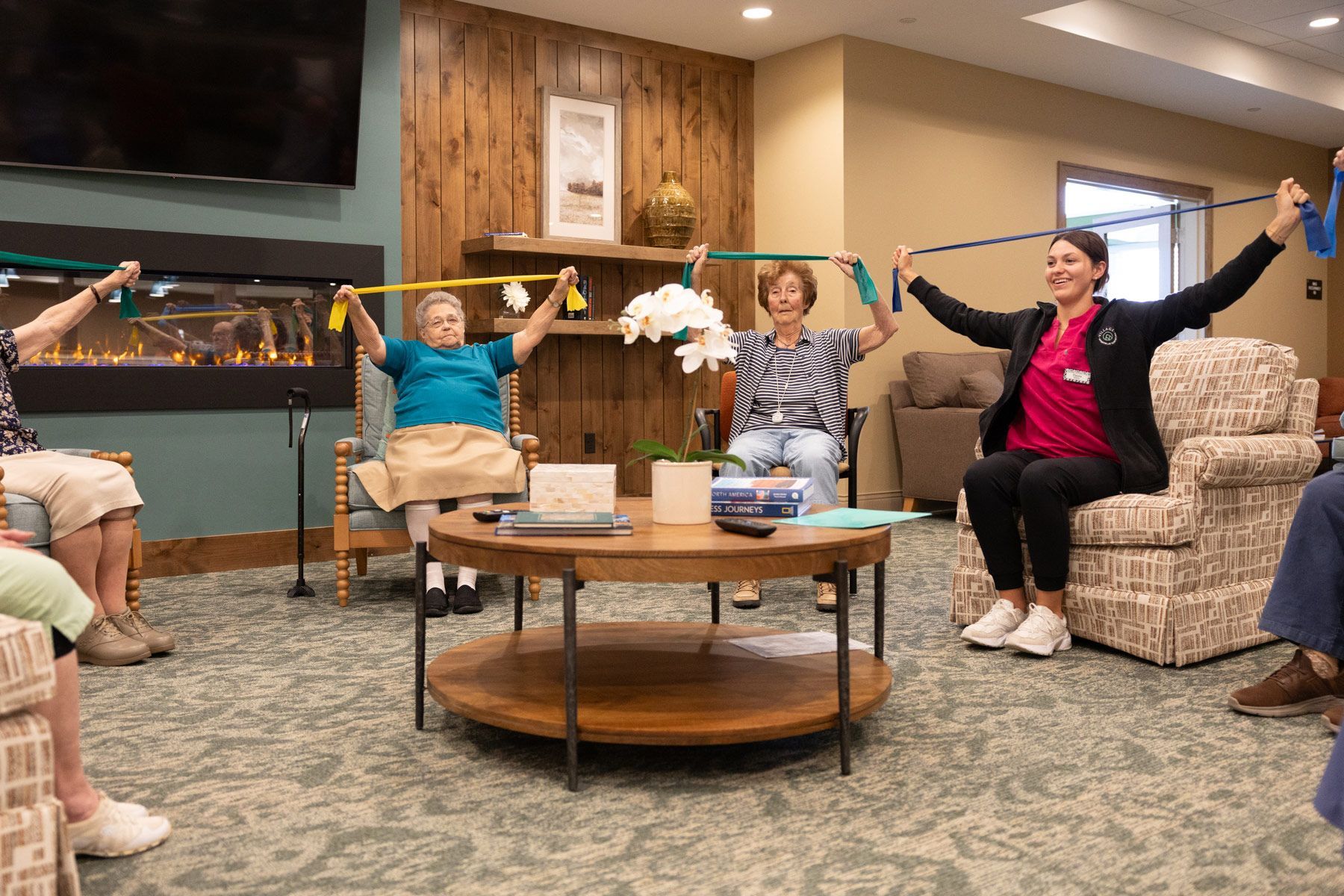 Group of people doing exercises with resistance bands in a living room setting, led by an instructor.