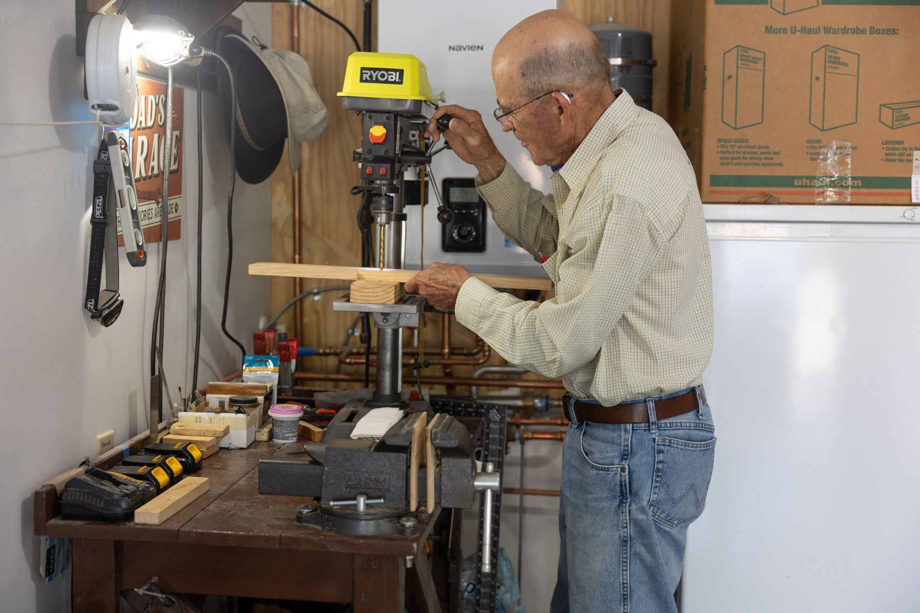 Man using a drill press in a workshop. He is drilling a hole in a wooden board.