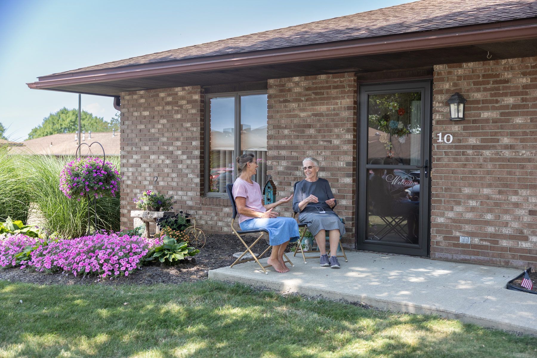 Two people sit outside a brick building under a porch.