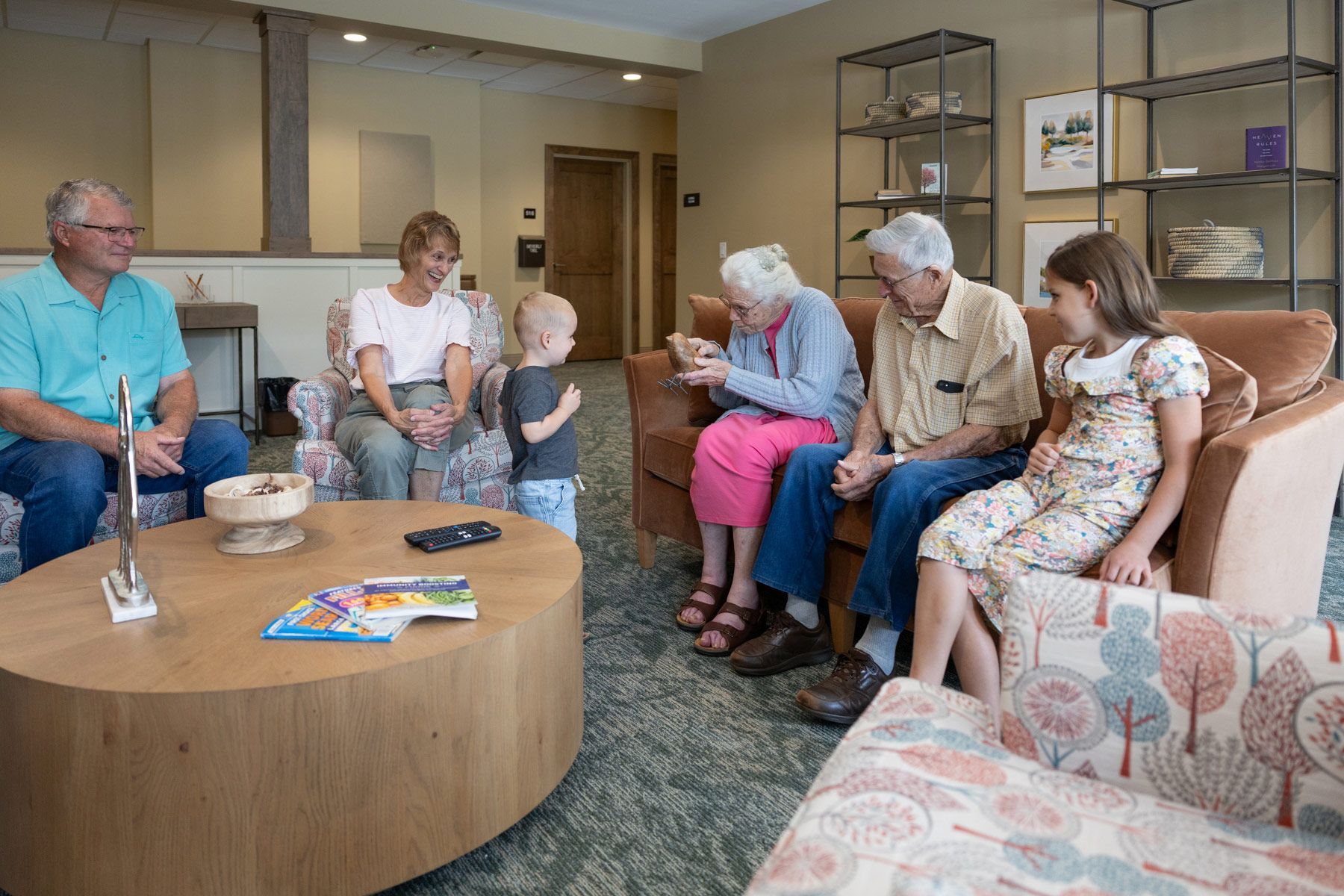 Family in living room: adults and children seated, interacting near a coffee table.