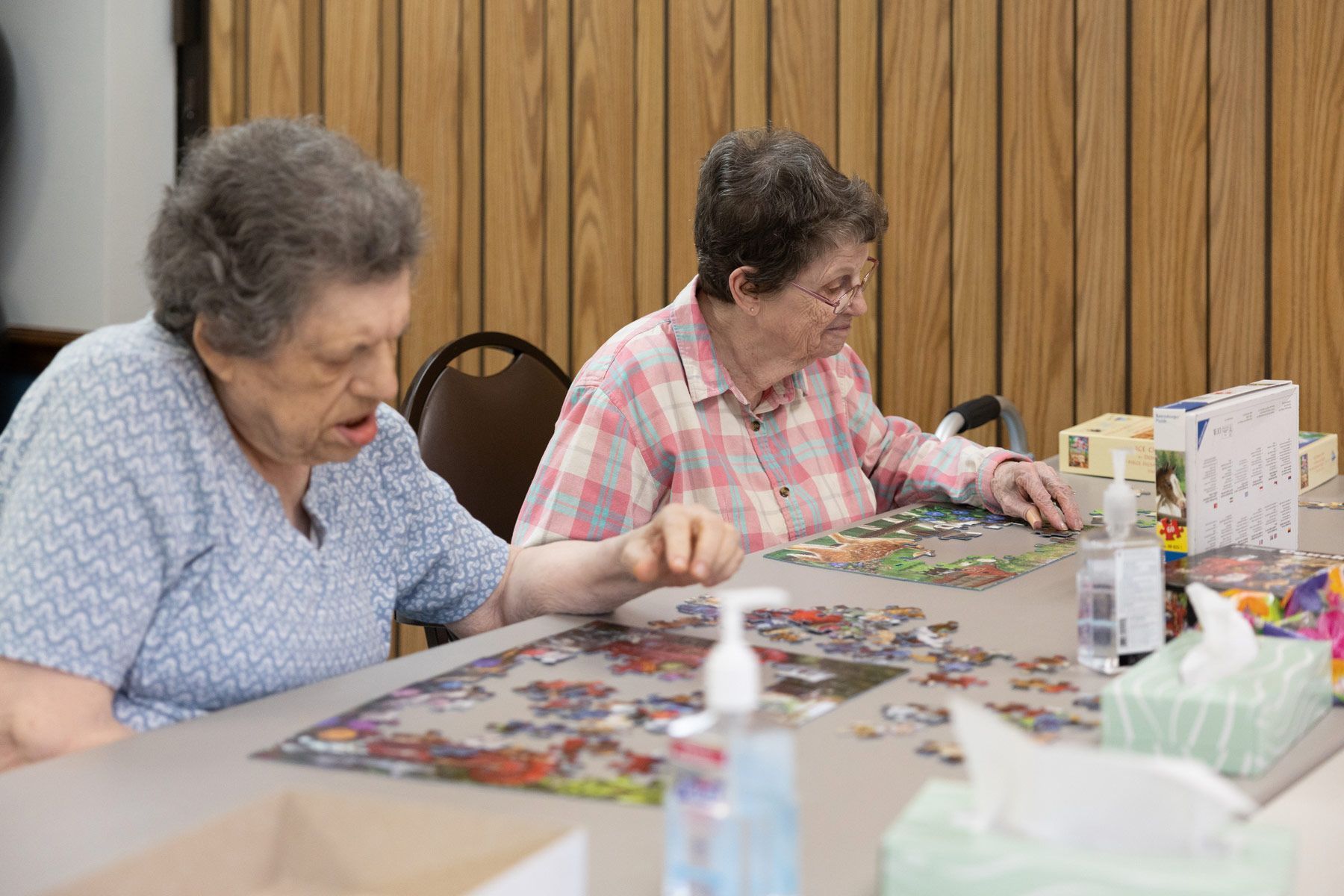Two people working on a jigsaw puzzle at a table in a room with wood paneling.