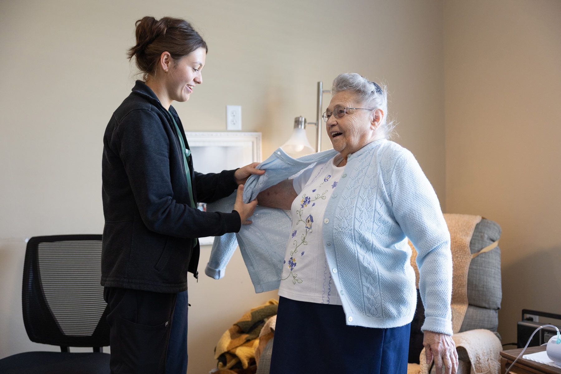 Woman helping an older person put on a light blue sweater indoors.