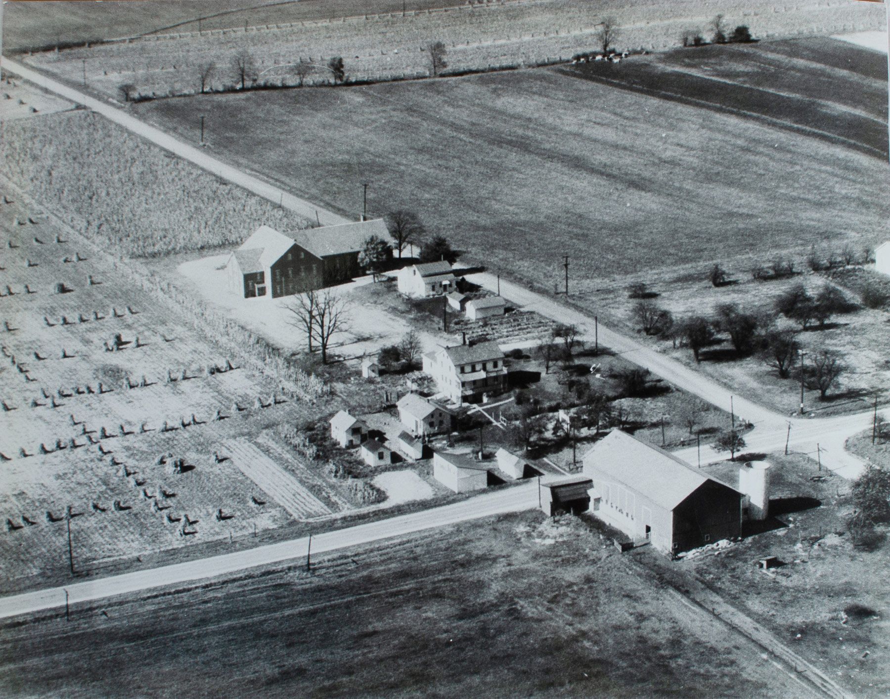 Aerial view of a rural village with buildings, roads, and fields. A cemetery is on the left.