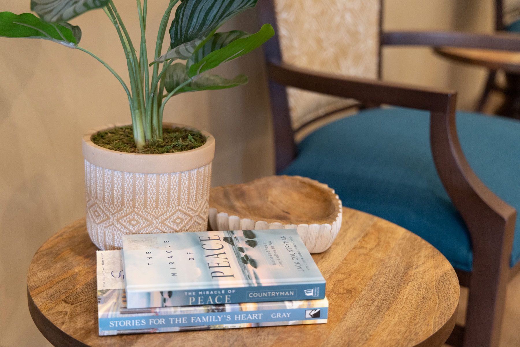 Wooden table with books and a potted plant next to a blue upholstered chair.