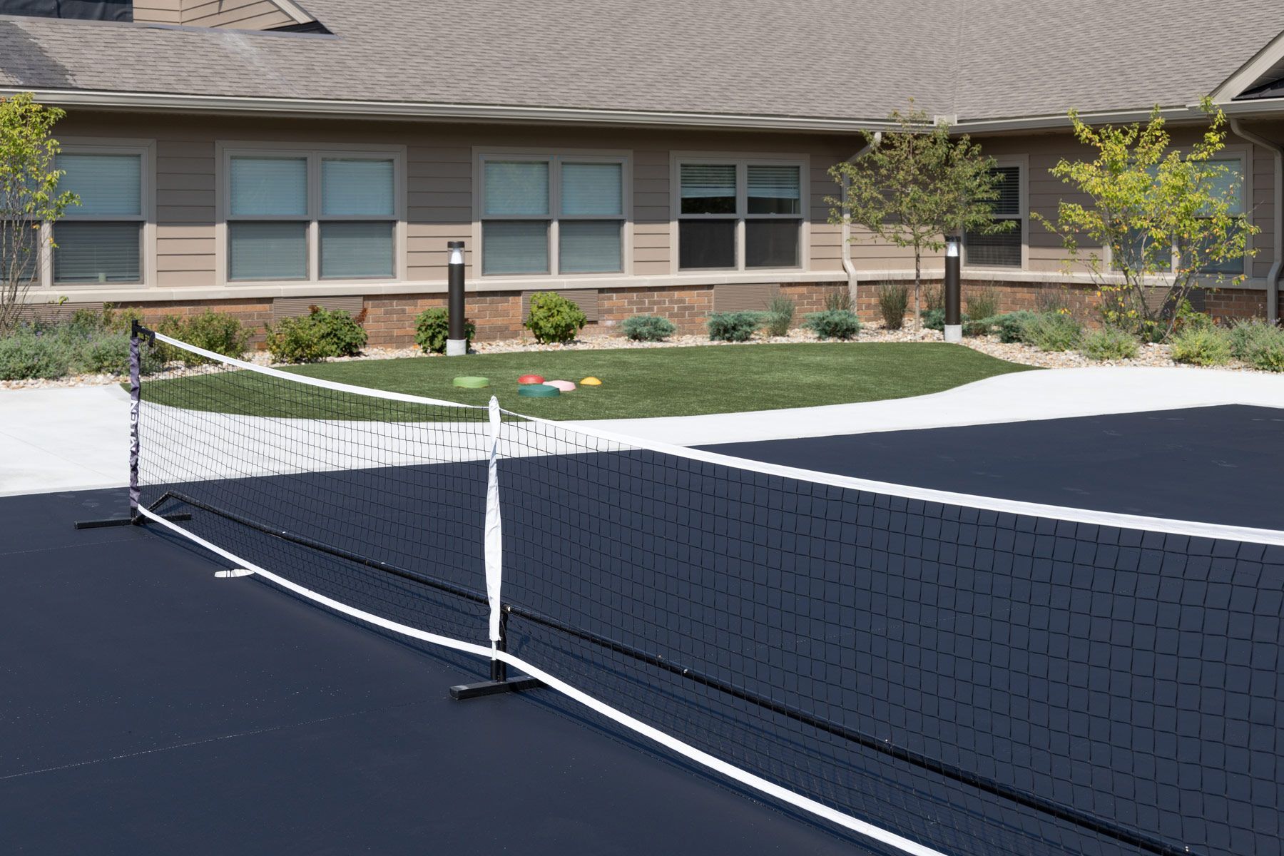 Tennis net on a dark court; green lawn and building in the background.